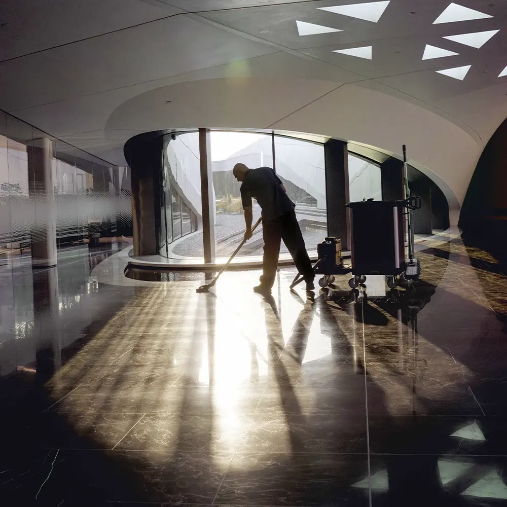 Reinigungskraft bei der Arbeit in einem futuristisch anmutenden, lichtdurchflutenden Büro